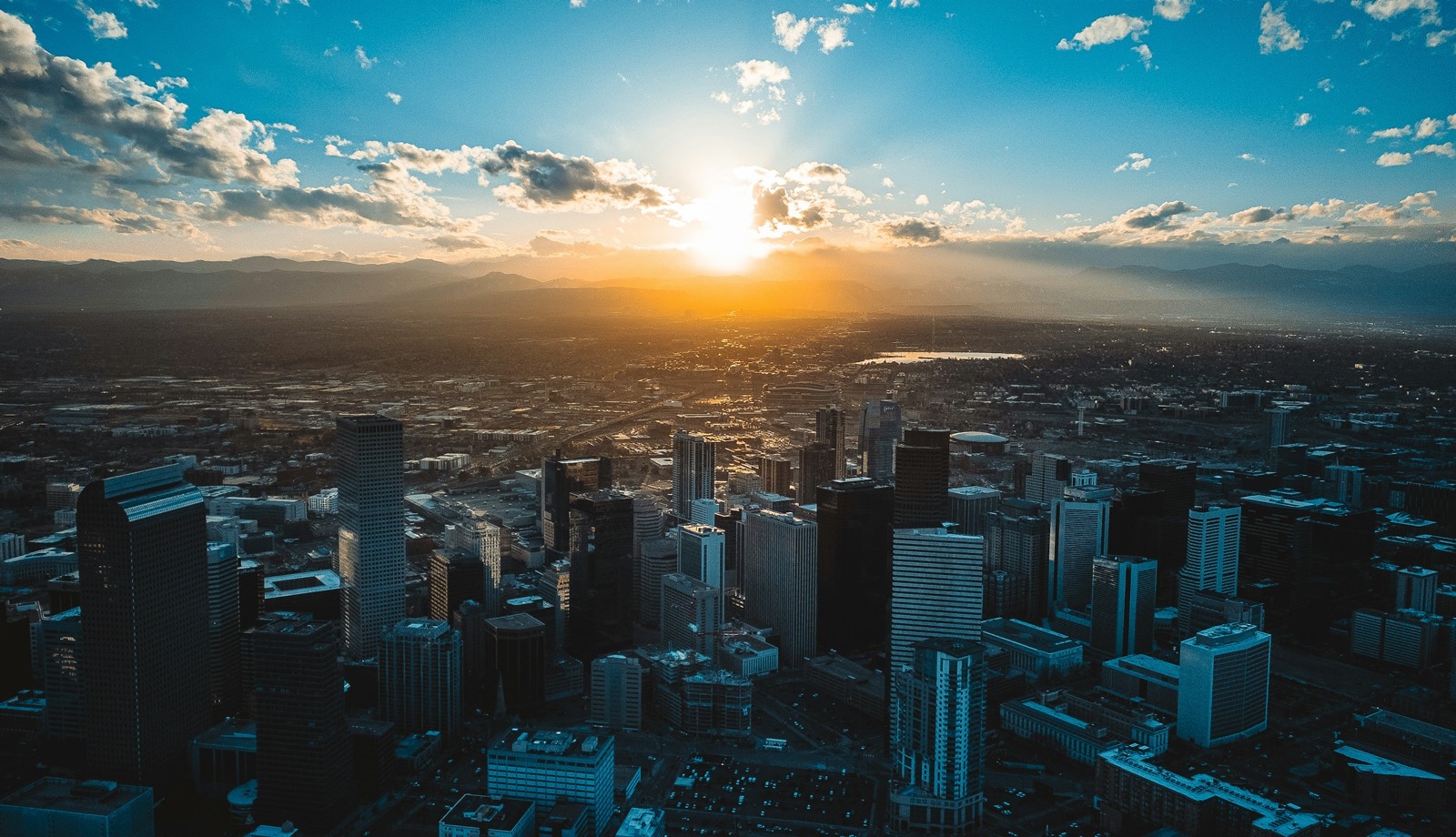 Aerial view of downtown Denver at sunset, with the Rocky Mountains along the horizon.